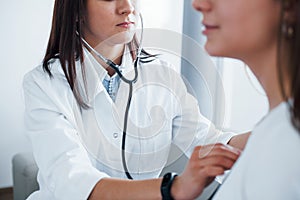 Using stethoscope. Young woman have a visit with female doctor in modern clinic