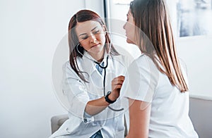 Using stethoscope. Young woman have a visit with female doctor in modern clinic