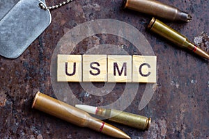 USMC sign with weapon bullets and army dog tags on rusty metal background. Military industry, United States Marine Corps concept