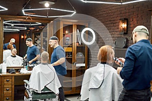 Usual day at barbershop. Two barbers working with clients in the modern barbershop