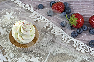 Usual vanilla cupcake with white cream with many strawberries and blueberries