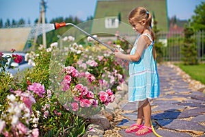 ?ute girl in blue dress watering flowers with a