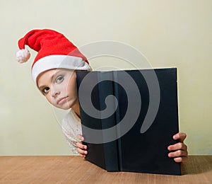 Ð¡ute girl in Santa Claus hat with big blue book.