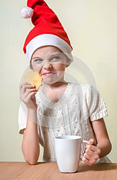 Ð¡ute girl in Santa Claus hat eat cookies.