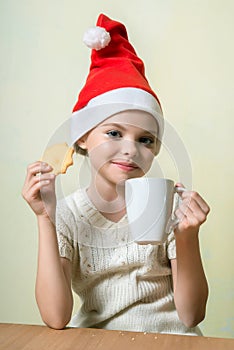 Ð¡ute girl in Santa Claus hat eat cookies.