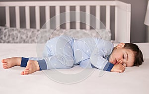 Ð¡ute little baby boy in light blue pajamas sleeping peacefully on bed at home.