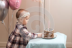 ute little girl blows out candles on a birthday cake at against backdrop of balloons. Child's birthday.