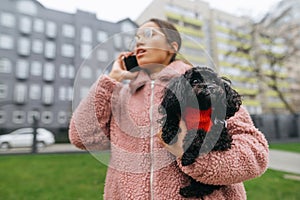 Ð¡ute puppy in the hands of an attractive girl talking on the phone in the city street, focus on the pet in the hands of the owner