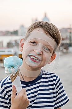 Ð¡ute seven-year-old boy in a striped t-shirt sits on the waterfront in Venice in the evening and eats gelato (ice cream