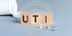 UTI - acronym from wooden blocks with letters, abbreviation UTI urinary tract infection, concept, grey background with ampoules