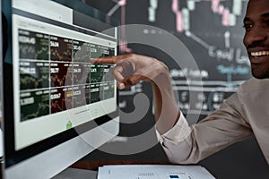 Utilising skills for earnings. African businessman, trader sitting in front of computer screen and looking at graph