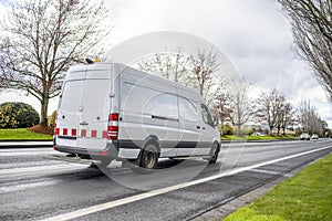 Utility cargo mini van with flashing light on the roof running on the straight local road at industrial area