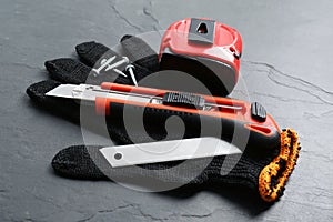 Utility knife, measuring tape and glove on black table, closeup