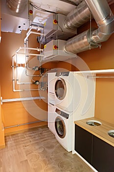 Utility room with two washing machines. There are large pipes on the ceiling