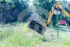 Utility workers are using a tractor mechanical mower to mow tall grass along the side of road near utility work site