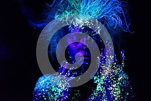 UV body art on the face of a very beautiful girl with a lush hairstyle on a dark background. Space figure.