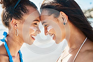 UV got a friend in me. two beautiful young women at the beach with sunscreen on their faces smiling at each other.