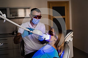 UV teeth whitening for woman patient in protective glasses in dentistry. Laser bleaching teeth in clinic. Dentist do