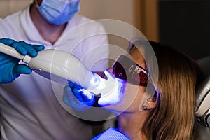 UV teeth whitening for woman patient in protective glasses in dentistry. Laser bleaching teeth in clinic. Dentist do