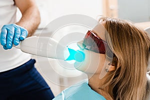 UV teeth whitening for woman patient in protective glasses in dentistry. Laser bleaching teeth in clinic. Dentist do