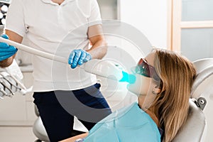 UV teeth whitening for woman patient in protective glasses in dentistry. Laser bleaching teeth in clinic. Dentist do