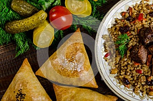 Uzbek national dish of pilaf and samsa on a dark wooden background with pickles