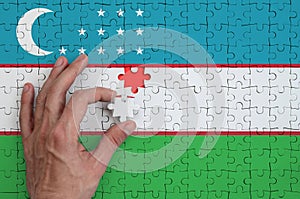 Uzbekistan flag is depicted on a puzzle, which the man`s hand completes to fold