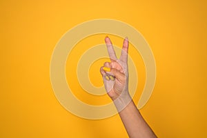 V sign. Female hand shows two fingers or peace gesture. Cut out on yellow background. Copy space