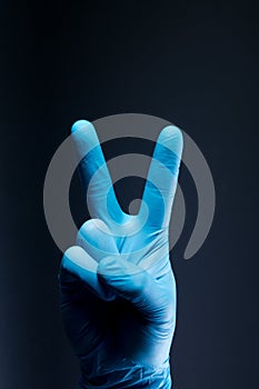 V sign is showed by right man hand in a blue medical glove on a black background. The symbol of Victory. Victory over a virus