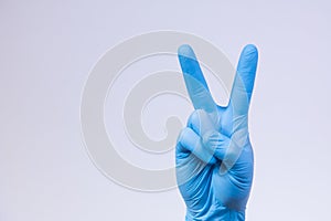 V sign is showed by right man hand in a blue medical glove on a white background. The symbol of Victory photo