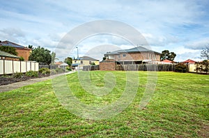 A vacant land with green grass/lawn surrounded by suburban houses in a Melbourne`s suburb. VIC Australia.