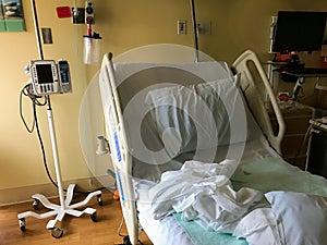 Vacant rumpled hospital bed with IV pole nearby photo