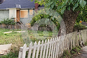 Vacant unkept yard with rickety fence and boarded up house photo