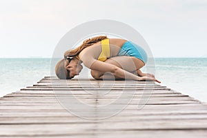 Vacation of Asian woman relaxing in yoga Child`s Pose stretching exercises muscle for warm up on pier with beautiful beach
