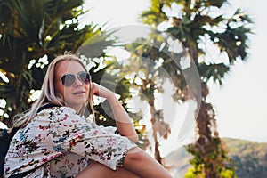 Vacation concept. Enjoying the summer. Young pretty woman in glasses sits on a palm tree over the ocean water.