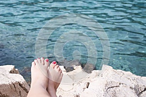 Vacation Concept. Tanning on the Beach. Woman`s Bare Feet over Sea background