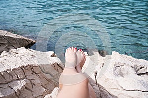 Vacation Concept. Tanning on the Beach. Woman`s Bare Feet over Sea background