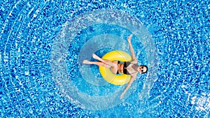 Vacation concept. Top view of slim young woman in bikini on the yellow air inflatable ring in the big swimming pool.