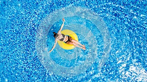 Vacation concept. Top view of slim young woman in bikini on the yellow air inflatable ring in the big swimming pool.