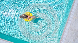 Vacation concept. Top view of slim young woman in bikini on the yellow air inflatable ring in the swimming pool