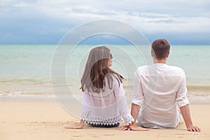 Vacation couple sitting on beach together in love holding around each other