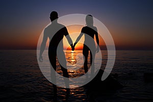 Vacation couple walking on sunset beach together in love holding hands. Happy young couple silhouette on sunset.