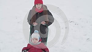 vacation, game, family concept - slo-mo authentic tired sad young mother pushes sled with toddler preschool son, older