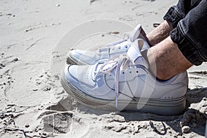 Vacation holidays. Close up of mans feet relaxing by the sea. White snikers