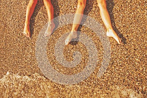 Vacation and holidays concept. Top view of feet of two young girls relaxing on beach enjoying sun and sea on sunny summer day