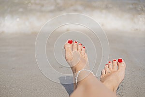 Vacation holidays. Woman feet closeup with red painted nails of girl relaxing on sunny summer day.