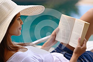 Vacation, relax and woman at pool with book, hat and lounge with happy summer travel on hotel patio. Holiday, deck chair