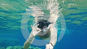Vacation at sea. A masked man with a tube floats near the surface of the water, waving his hand at the camera