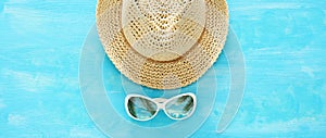Vacation and summer banner with fedora beach hat and sunglasses over blue wooden background.
