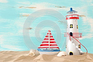 Vacation and summer concept with vintage boat, starfish, lighthouse and seashells over beach sand infront of pastel blue